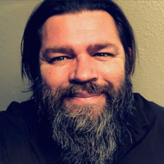 Brett Petersen headshot - fair-skinned man, smiling, black hair, gray beard, black shirt