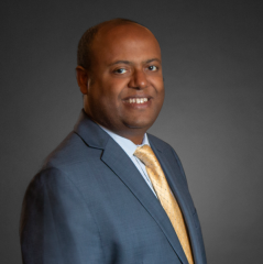 Kassaw Merie headshot - dark-skinned man, smiling, brown hair, white collared shirt, gray blazer, gold tie