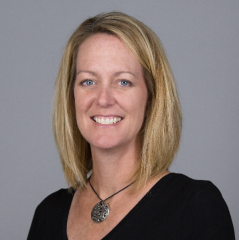 Melanie O’Neil headshot - fair-skinned woman, smiling, blonde hair, black shirt, necklace 